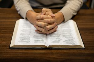 A person sitting at a table with their hands folded over a book