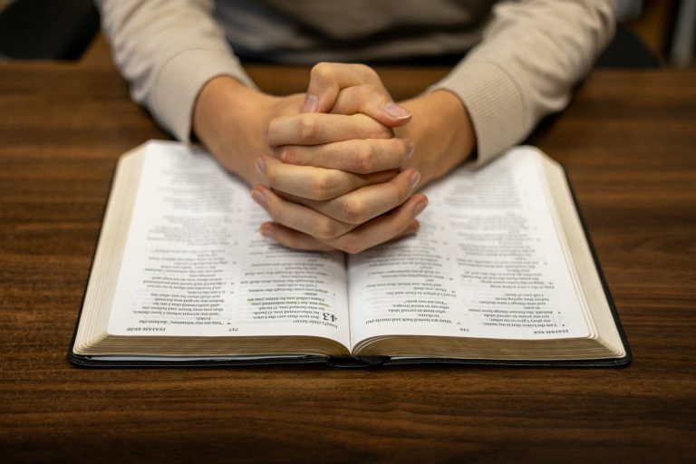 A person sitting at a table with their hands folded over a book